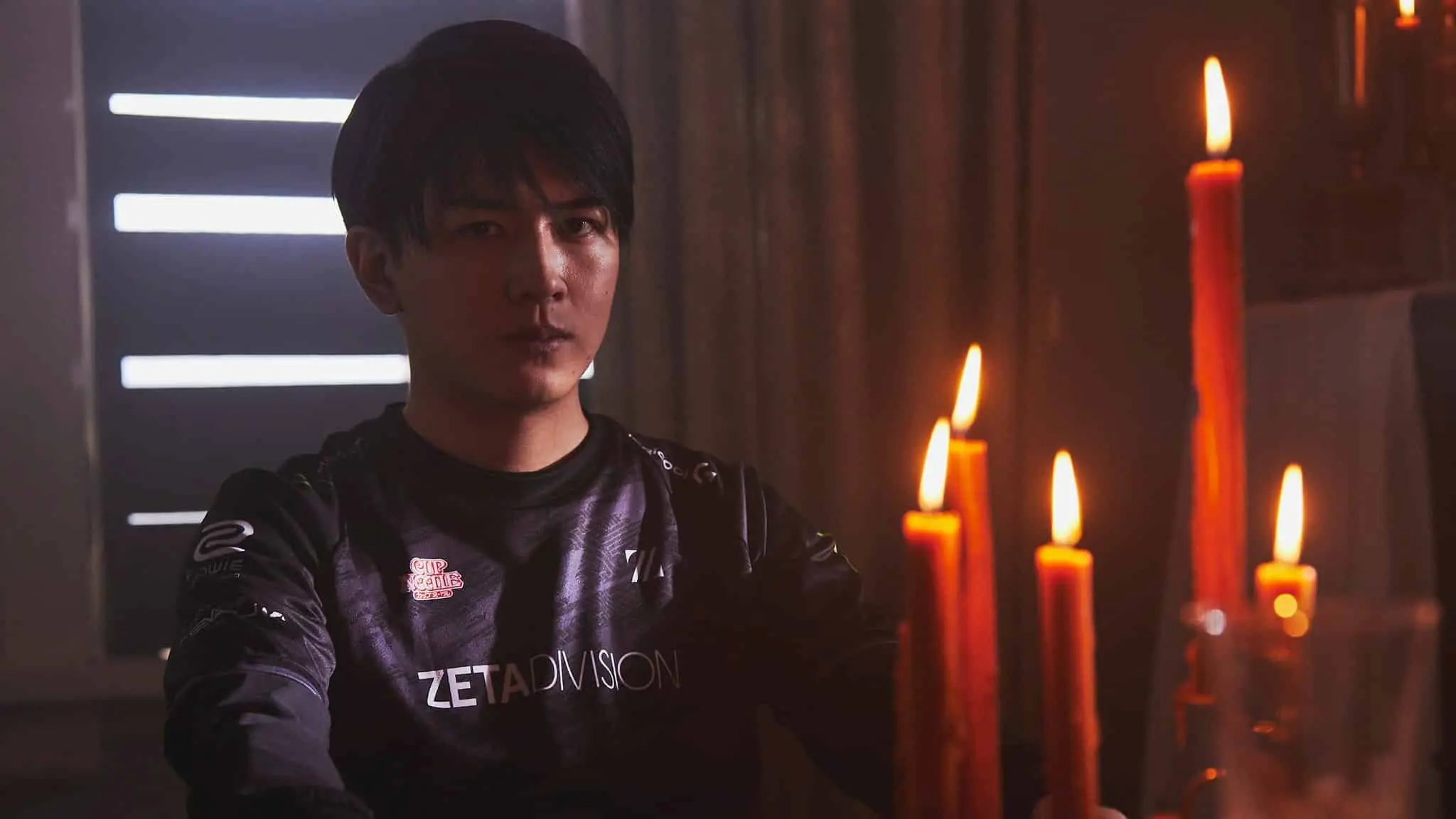 Laz stares into the camera intently while sitting in front of candles.