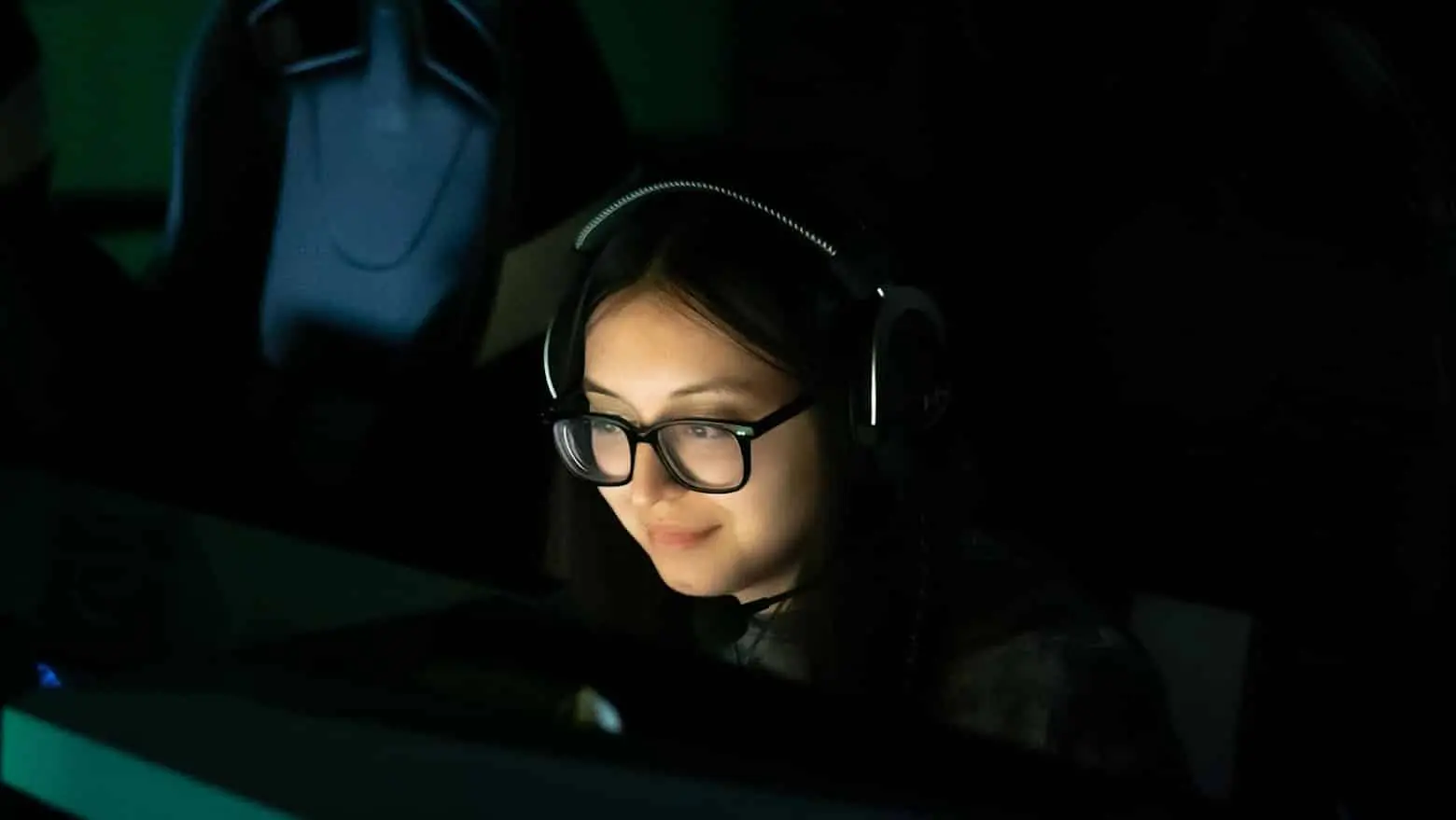 MeL in all black with her face lit up by a computer screen 