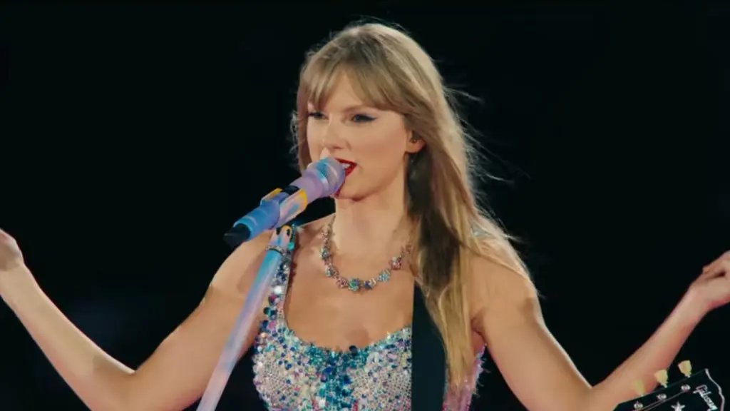 Taylor Swift performing onstage with an acoustic guitar at a concert.