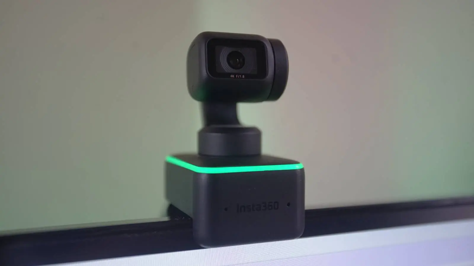 A close up shot shows the Insta360 Link Webcam, a matte black web camera on a gimbal, with green lights running around a cube base