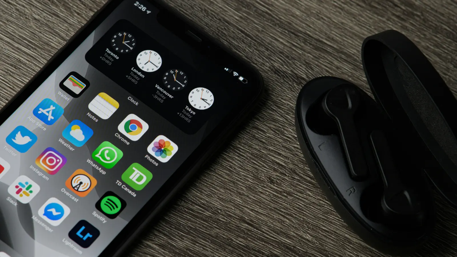 An iPhone placed in a wooden table next to earphones