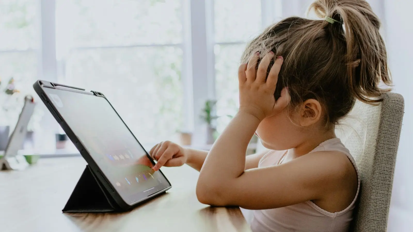 A child sitting by a table with a tablet in front of her