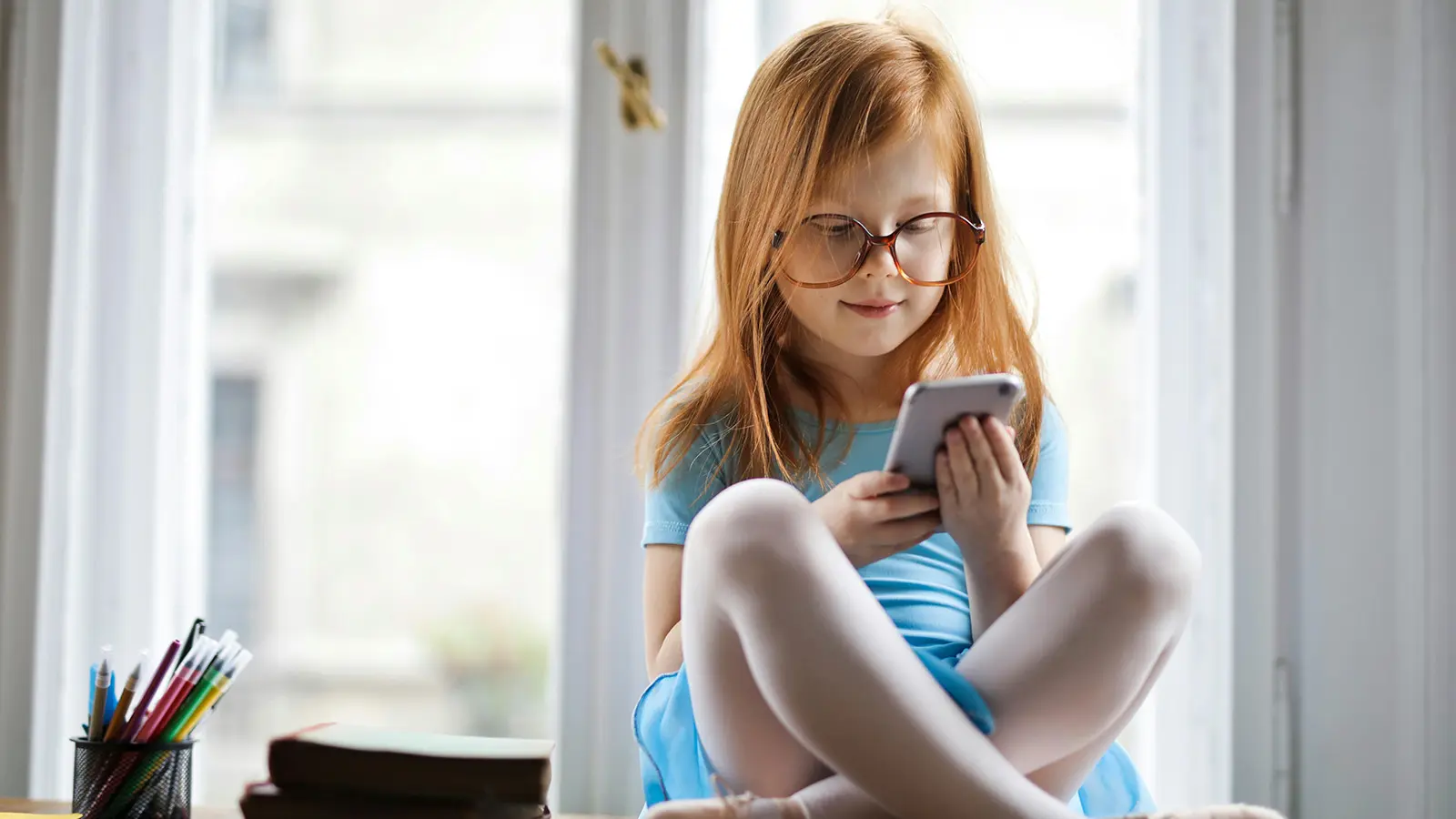 kid sitting on a desk looking at a phone