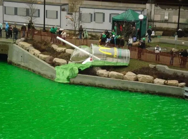 A giant shamrock shake sculpture spilling into a river dyed green.