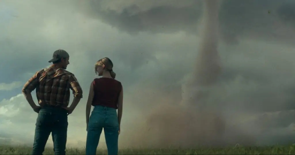 Glen Powell and Daisy Edgar-Jones as Tyler and Kate, standing in a field and staring at a twister in Twisters