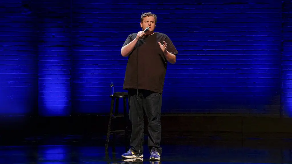 Tim Dillon standing on stage against a blue curtain