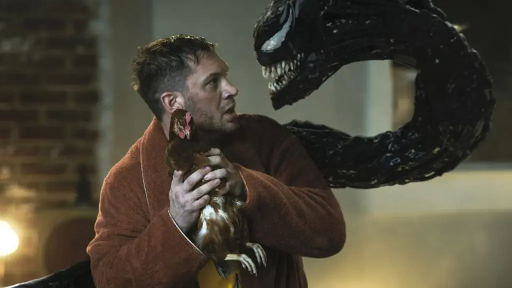 Tom Hardy as Eddie Brock, holding a chicken while Venom looks at him