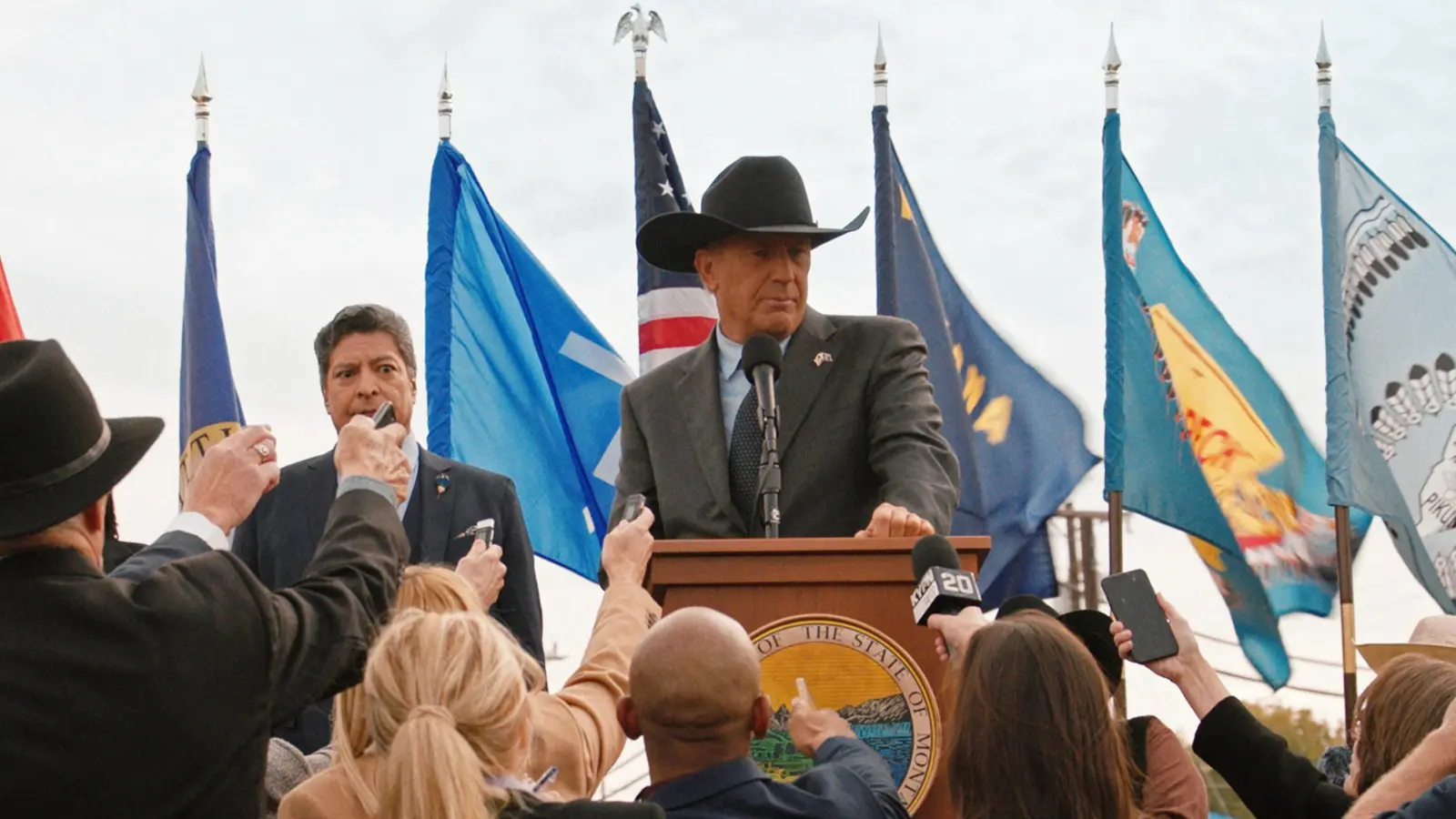 Kevin Costner as John Dutton in Yellowstone standing behind a podium