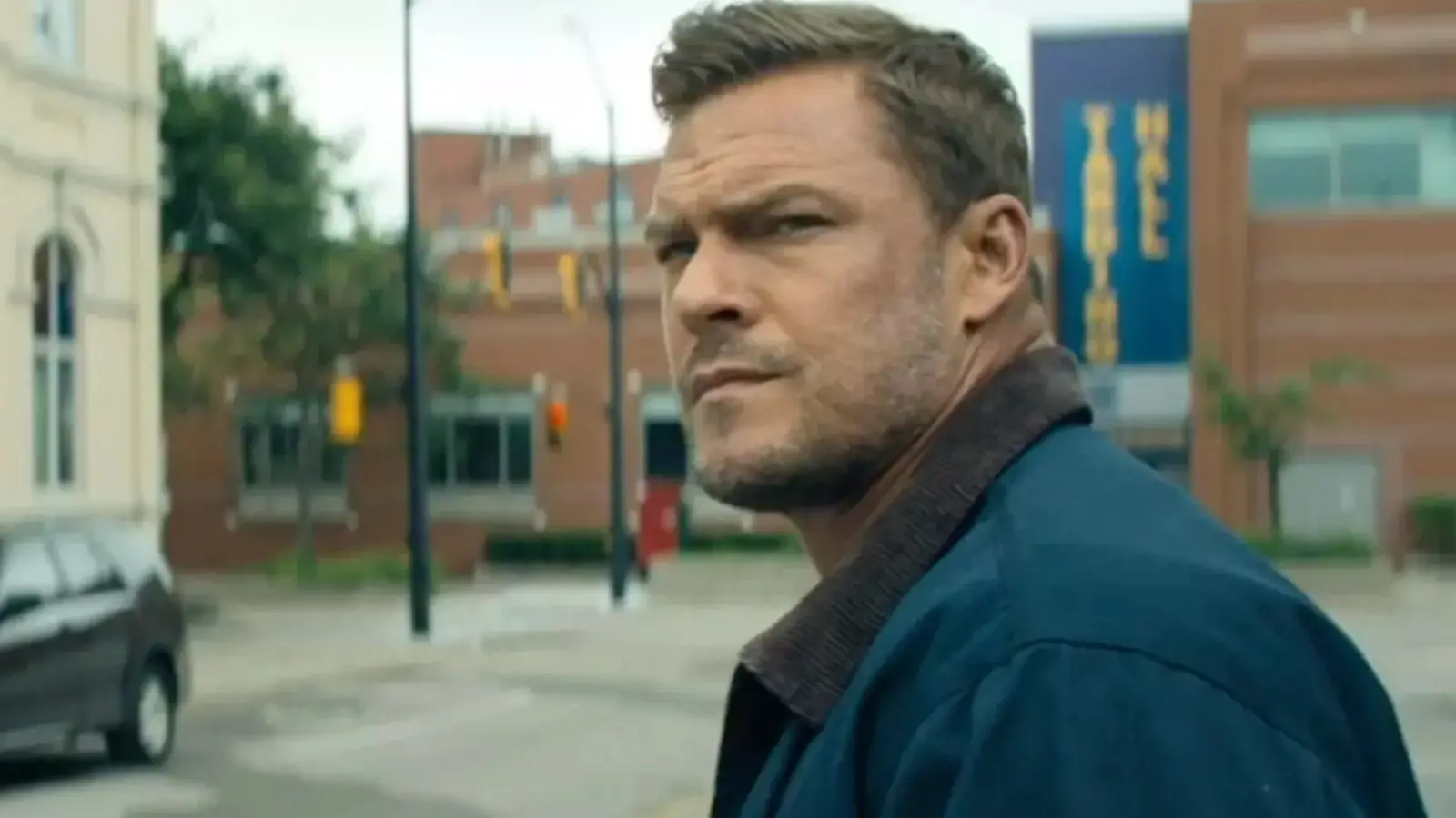 Alan Ritchson looking down a street suspiciously in Season 3 of Reacher.